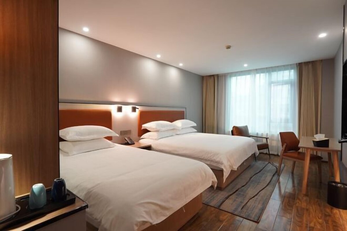 A hotel room with two beds, a desk, a chair, and a television.