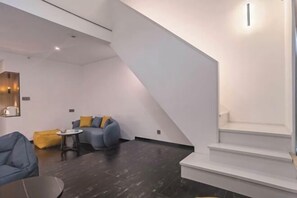 A modern living room with dark flooring, a staircase, and a seating area with blue sofas and yellow cushions. - Jinglan Yipin Hotel (Jingdezhen Taoxichuan Branch) (Jingdezhen)