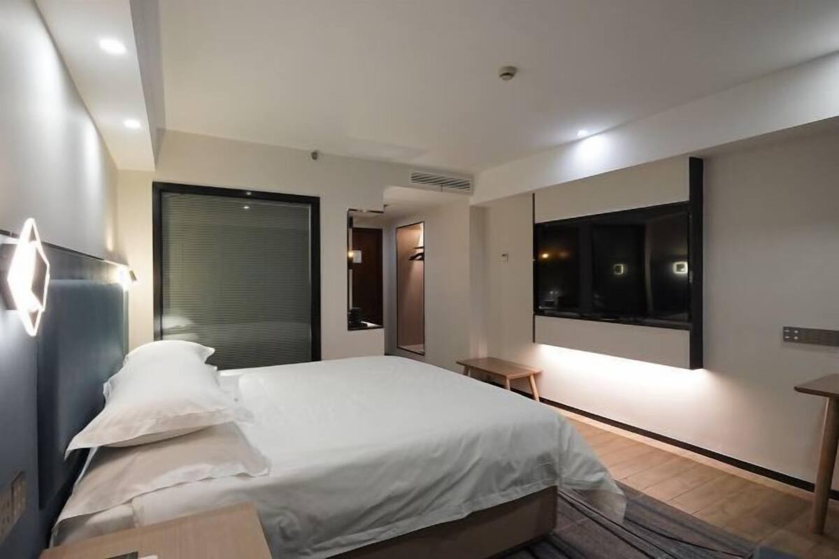 A modern hotel room with a large bed, a bedside table, a mirror, and a TV.