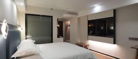 Une chambre d’hôtel moderne avec un grand lit, une table de chevet, un miroir et un téléviseur.