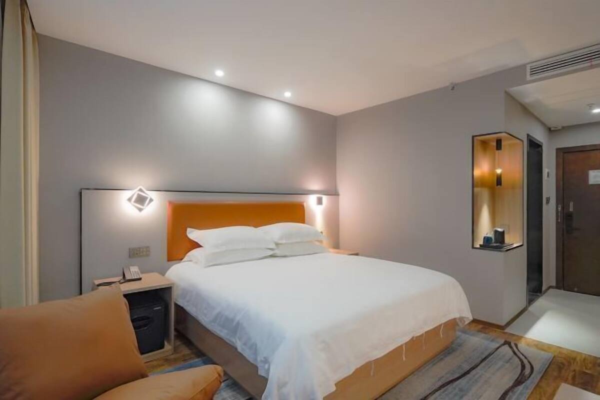 A modern hotel room with a large bed, a nightstand, a chair, and a mirror.