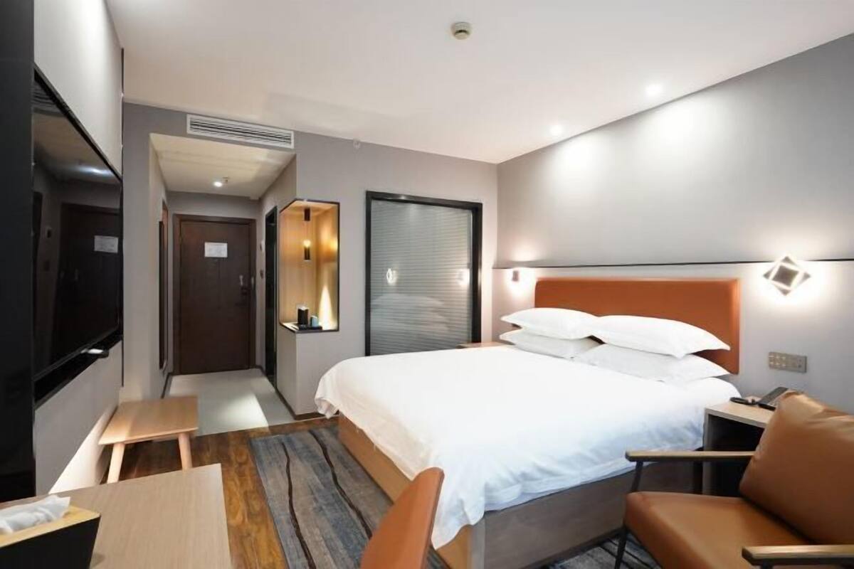 A hotel room with a bed, a desk, a chair, a TV, and a door.