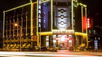 Fachada luminosa de un hotel con señalización iluminada, una entrada destacada y una vista despejada de la calle.