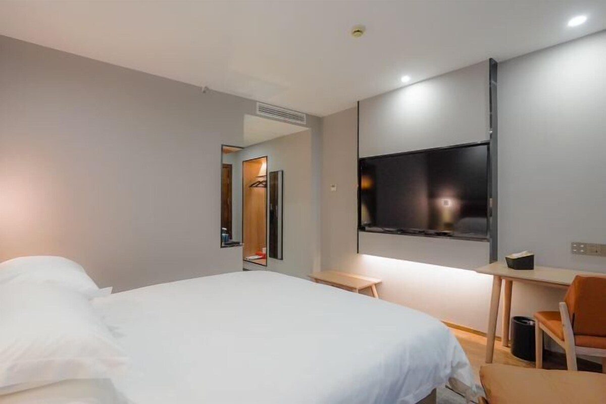 A modern hotel room with a bed, a desk, a chair, a TV, and a mirror.
