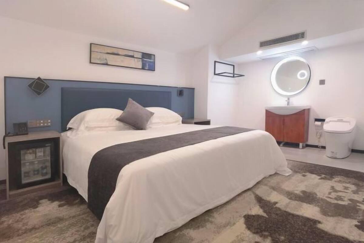 A bedroom with a bed, bedside tables, a mirror, a vanity, and a toilet.