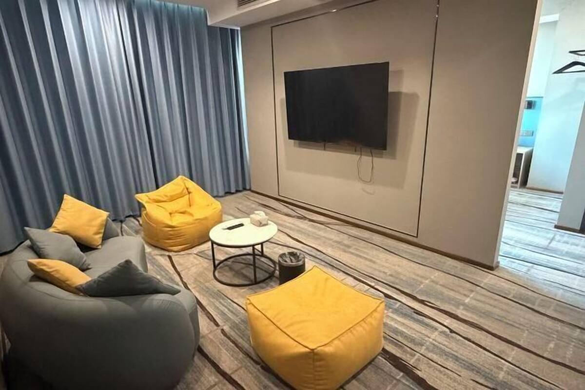 A modern living room with a sofa, two yellow bean bags, a small round table, and a flat-screen TV mounted on the wall.