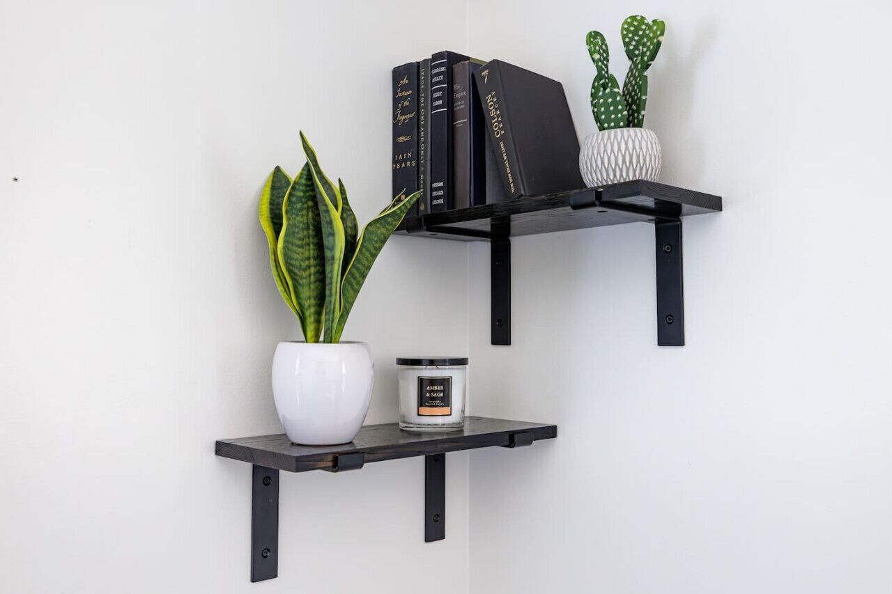 A black metal shelf with a potted plant, a white vase, and a candle.