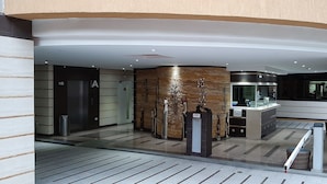 Een moderne lobby met een receptiebalie, een glazen lift en een trap die naar een verdieping leidt.