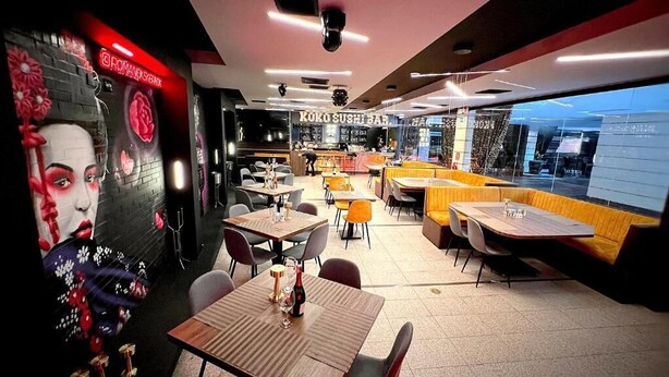 Een restaurant met tafels en zitplaatsen, een sushi bar op de achtergrond, en een muurschildering.
