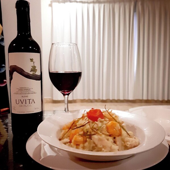 A bottle of Uvita de Plata wine and a glass of red wine next to a plate of food. - Novo Hotel (Caracas)