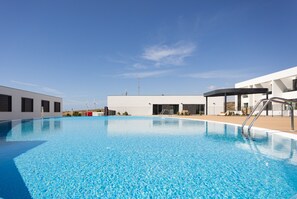 A modern pool area with clear blue water, a covered seating area, and a building with large windows and a flat roof.