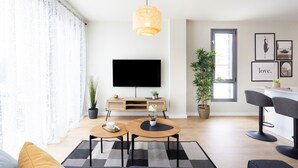 A modern living room with a flat-screen TV, two round tables, a sofa, a bar area, and potted plants.