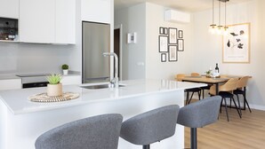 A modern kitchen with white cabinetry, a central island with bar stools, a dining area with a wooden table and chairs, and a wall with framed artwork.