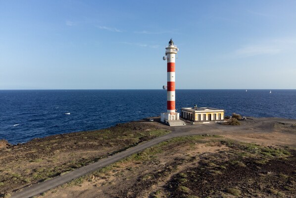 A tall lighthouse with a red and white striped tower, situated on a rocky coastline with a clear view of the ocean.