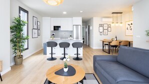 A modern living room with a grey sofa, a wooden coffee table with a plant, and a kitchen area with white cabinets and a central island.