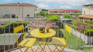 Un balcon avec des chaises jaunes et une table, donnant sur un quartier résidentiel avec des maisons et de la verdure.