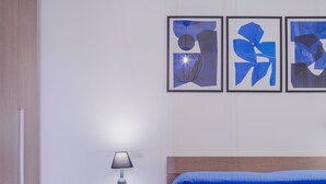 Une chambre à coucher avec un lit, une table de chevet, une lampe et trois tableaux abstraits accrochés au mur.