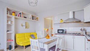 Une cuisine de taille réduite avec des meubles blancs, un canapé jaune et une table à manger avec des chaises.