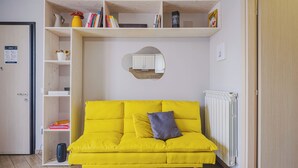 Un canapé jaune vif agrémenté d’un coussin, un radiateur blanc et une porte en bois.