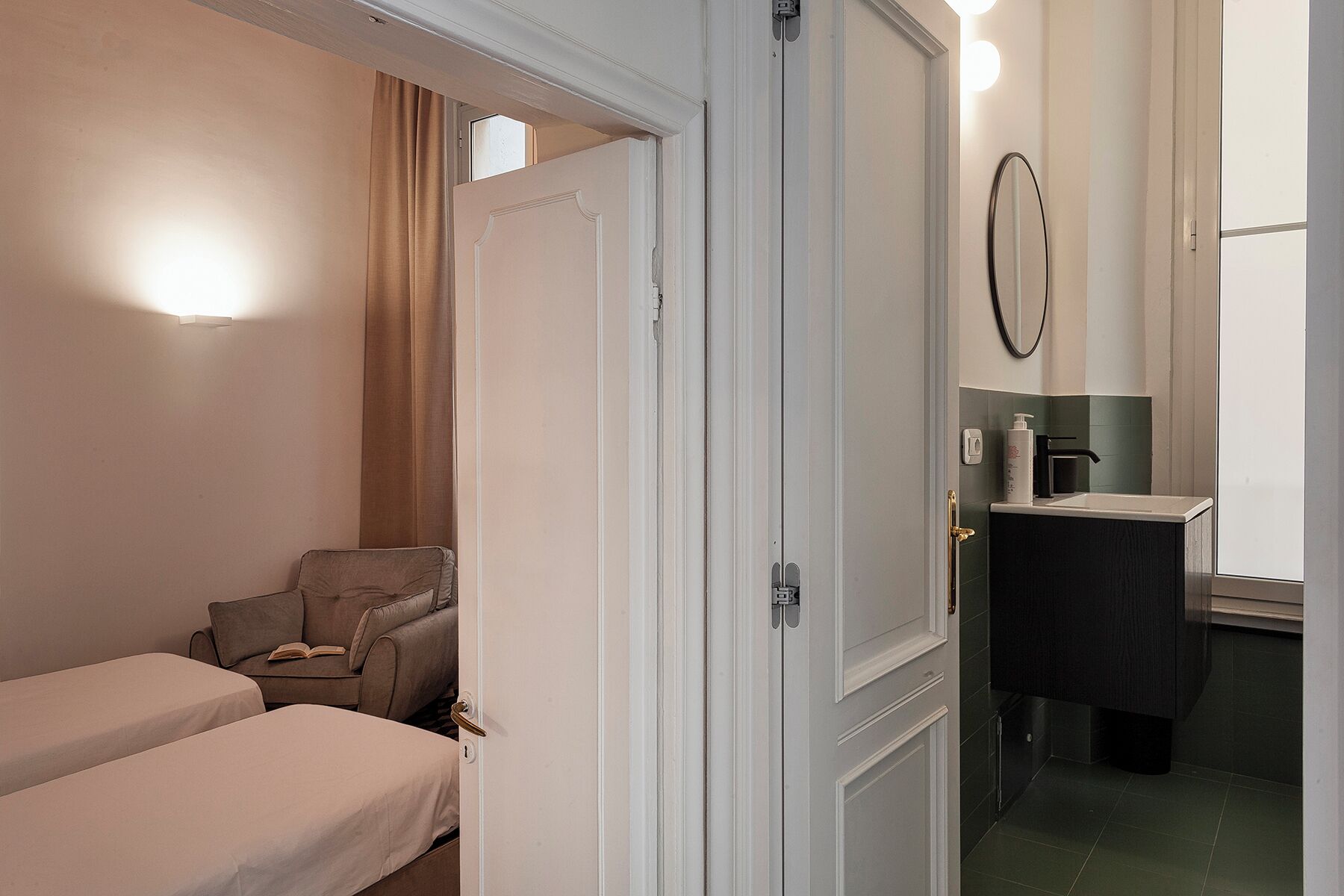 Camera d'albergo con due letti, un'area salotto, un bagno con specchio e una finestra.