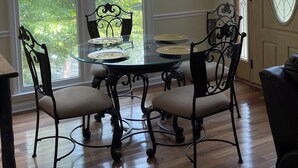A dining area with a glass table and chairs, a hanging light fixture, and large arched windows with greenery outside. - River tunes at its best panoramic views just steps away from the river  (Ellijay)
