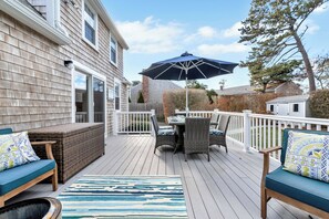 A deck with outdoor furniture, a table, and a large umbrella. - Beach Bungalow: Steps to Beach, Luxury Family Fun (Harwich)