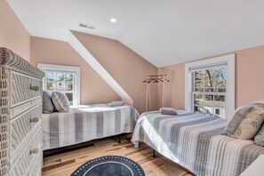 A bedroom with two beds, a wooden floor, a large window, and a hanging clothes rack. - Beach Bungalow: Steps to Beach, Luxury Family Fun (Harwich)
