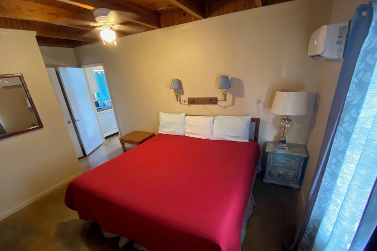 Un dormitorio con una cama grande, techo de madera, mesita de noche con lámpara y aire acondicionado de pared.
