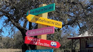 A directional signpost with multiple colorful arrows pointing to various amenities such as a general store, RV pull-thru sites, and cabins. - Hi-Line Lake Resort (Tow)