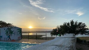 A swimming pool with a sunset view, a mural of palm trees, and flags on poles. - Hi-Line Lake Resort (Tow)