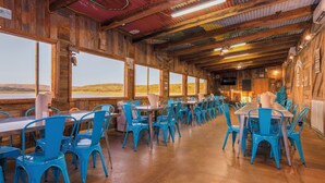 A restaurant with wooden walls and blue chairs, large windows, and a view of the landscape. - Hi-Line Lake Resort (Tow)