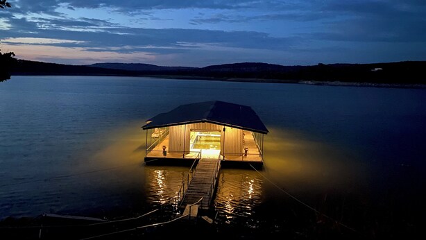 A houseboat with a dock, surrounded by calm water and distant hills. - Hi-Line Lake Resort (Tow)