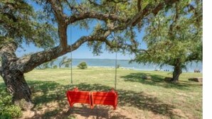 A swing under a large tree by a lake. - Hi-Line Lake Resort (Tow)