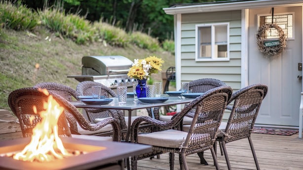 Un espace extérieur aménagé pour les repas, avec des chaises en osier, une table avec des assiettes et des verres, un foyer et un barbecue.
