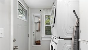 Une petite buanderie équipée d’un lave-linge, d’un sèche-linge et d’une petite fenêtre avec des stores.