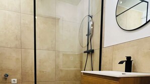 Et badeværelse med en glasafskærmet brusekabine, et træbord og et hvidt toilet.