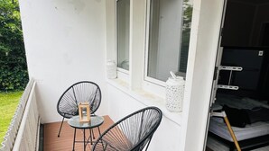En balkon med to sorte stole i wireframe-design, et lille bord og en hvid væg med vinduer.