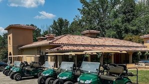 Eine Reihe von grünen Golfcarts auf einem Kiesparkplatz, im Hintergrund ein Gebäude.