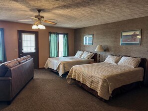 A hotel room with two beds, a ceiling fan, a lamp, a couch, and a door. - Quad Deluxe Cabin -Bungalow w/ Two Kitchens & 4 Bedrooms! (Golconda)