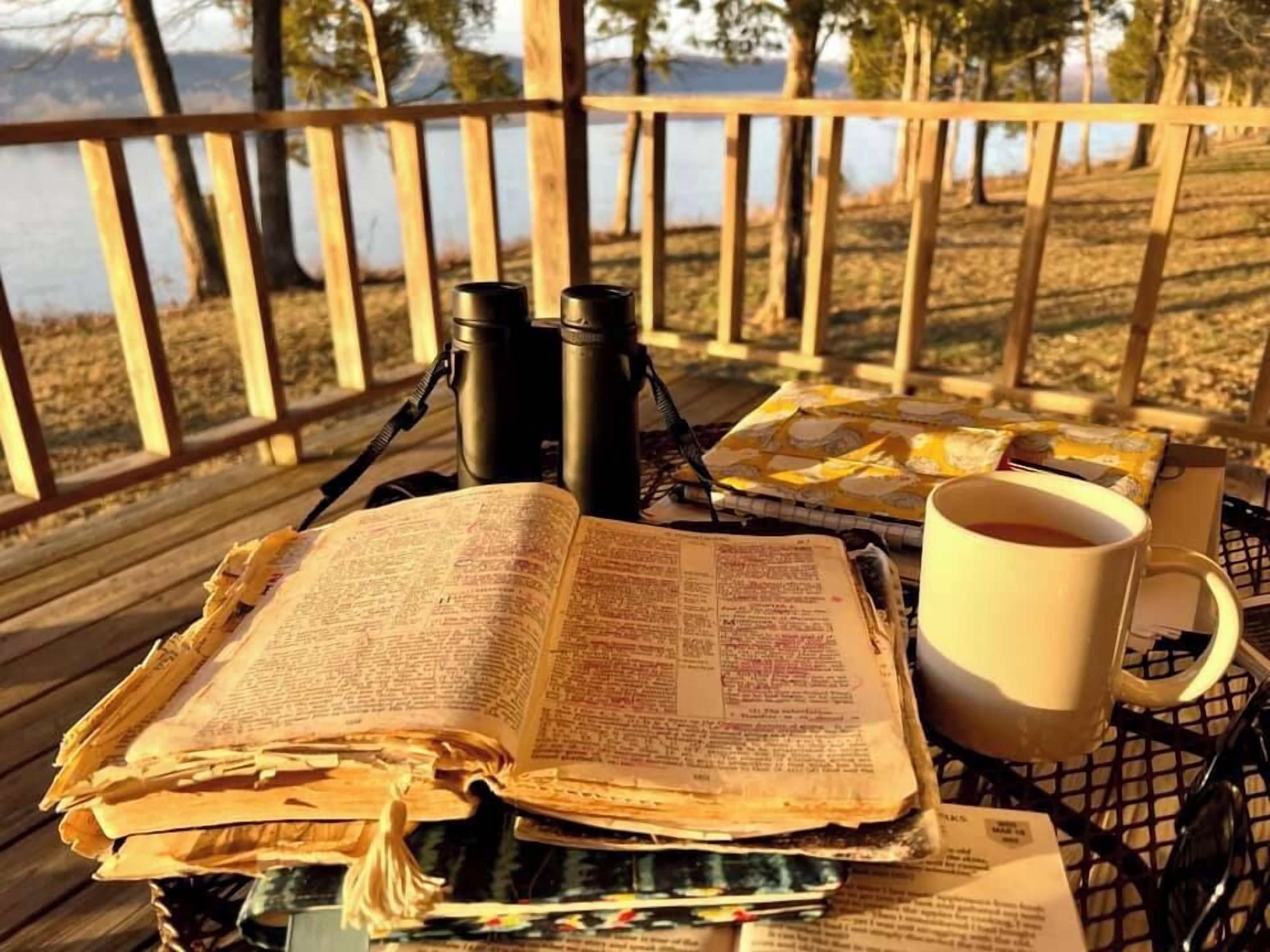 Un libro abierto sobre una mesa, junto a una taza y unos binoculares.