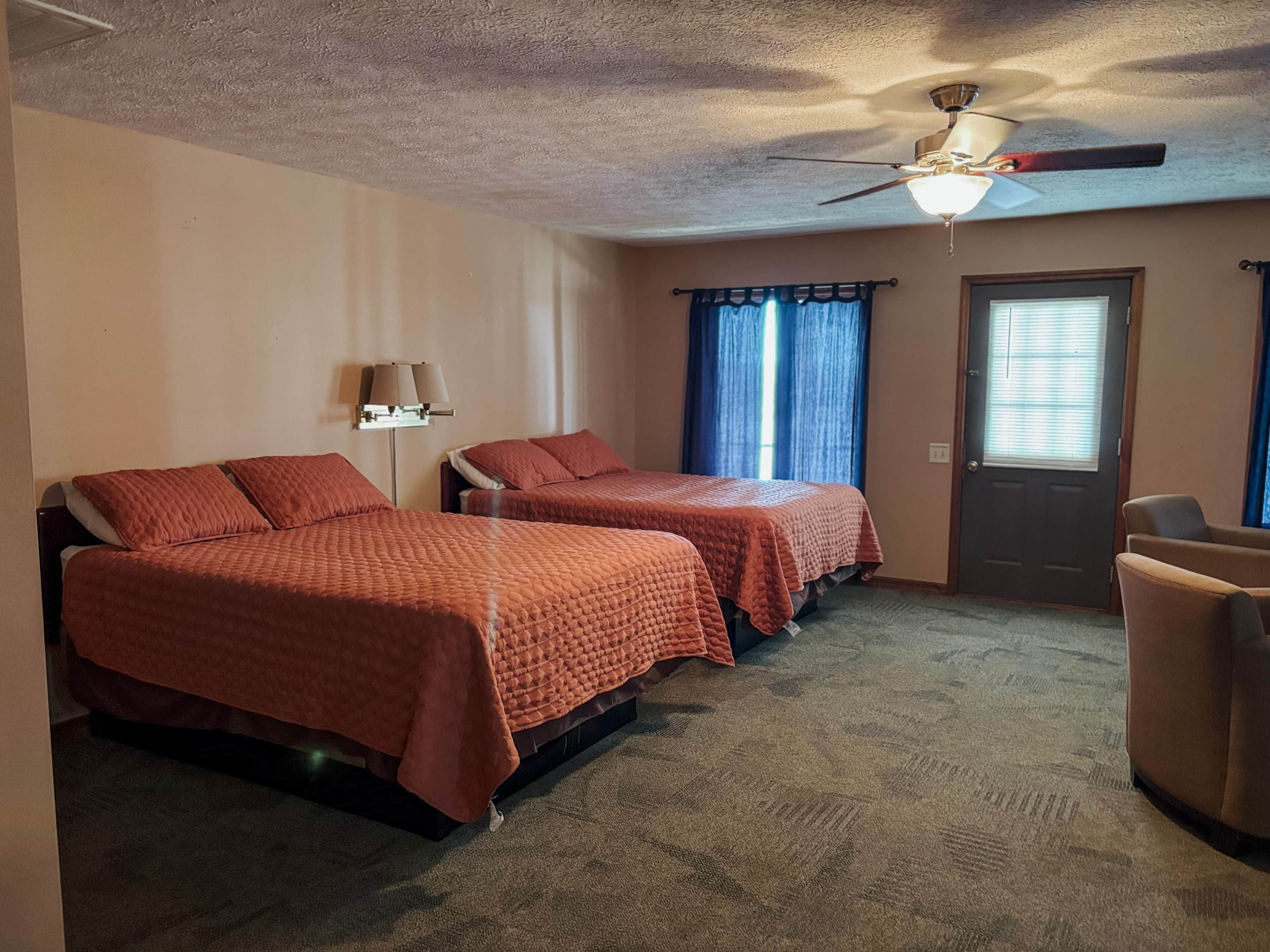 A hotel room with two beds, a ceiling fan, a door, and a window with curtains.