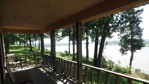 A wooden deck with a railing, overlooking a lake with trees and grassy areas. - Deluxe Suite - Bungalow overlooking the River! (Stone Church Precinct)
