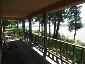 Une terrasse en bois dotée d’une rambarde, qui offre une vue sur un lac bordé d’arbres et de zones verdoyantes.