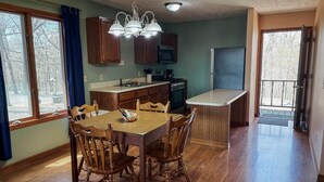 A dining area with a wooden table and chairs, a kitchen with a refrigerator and stove, and a view through a window. - Deluxe Suite - Bungalow overlooking on the Bluff! (Stone Church Precinct)