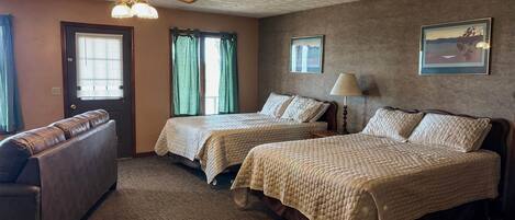 A hotel room with two beds, a ceiling fan, a lamp, a couch, and a door.