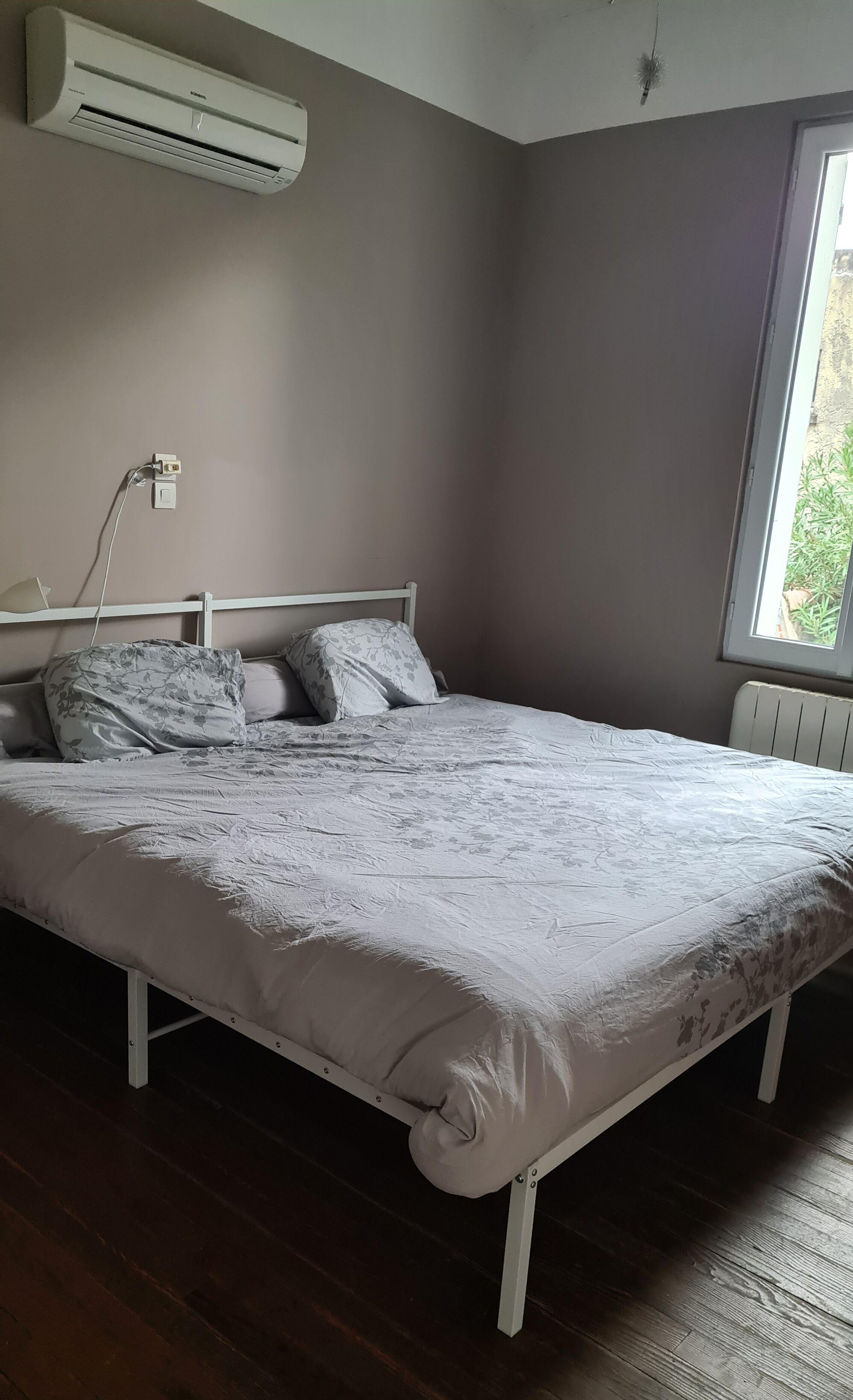 Un dormitorio con cama, aire acondicionado, ventana y radiador.