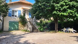 A house with a staircase leading to a green door, surrounded by trees and a gravel driveway. - Maison Avec Jardin Clôt (Montélimar)