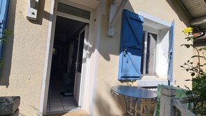 A building entrance with a door leading inside, a small outdoor table, and a blue shuttered window. - Maison Avec Jardin Clôt (Montélimar)