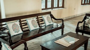 A room with a wooden bench and matching chairs, each with floral-patterned cushions. A small table with a woven placemat and a book is in front of the bench. - Urban Trippers Shamiyana Villa byArindam (Jaipur)