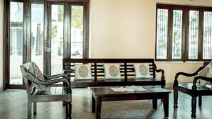 A room with a wooden bench, two chairs, a coffee table, and large windows with bars. - Urban Trippers Shamiyana Villa byArindam (Jaipur)